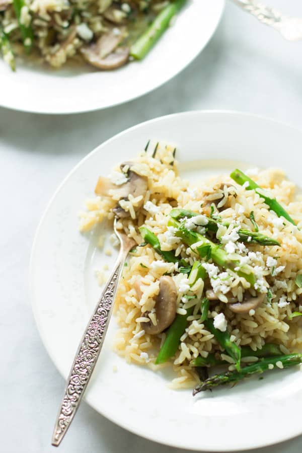 Close up of a plate of rice with mushroom and asparagus with a fork.