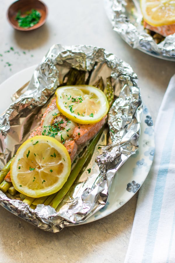 A plate with photo of a foil baked salmon overtop asparagus inside of the foil packet.