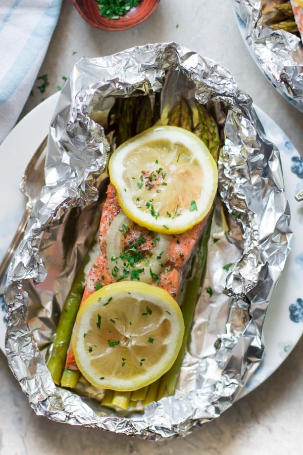 A plate with salmon with lemon slices overtop a bed of asparagus inside of tin foil.