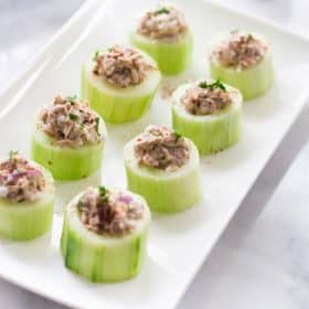 Cucumber cups full of tuna salad arranged on a white rectangular serving tray.