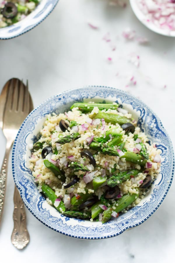 A bowl of asparagus couscous salad with a fork and spoon beside it.