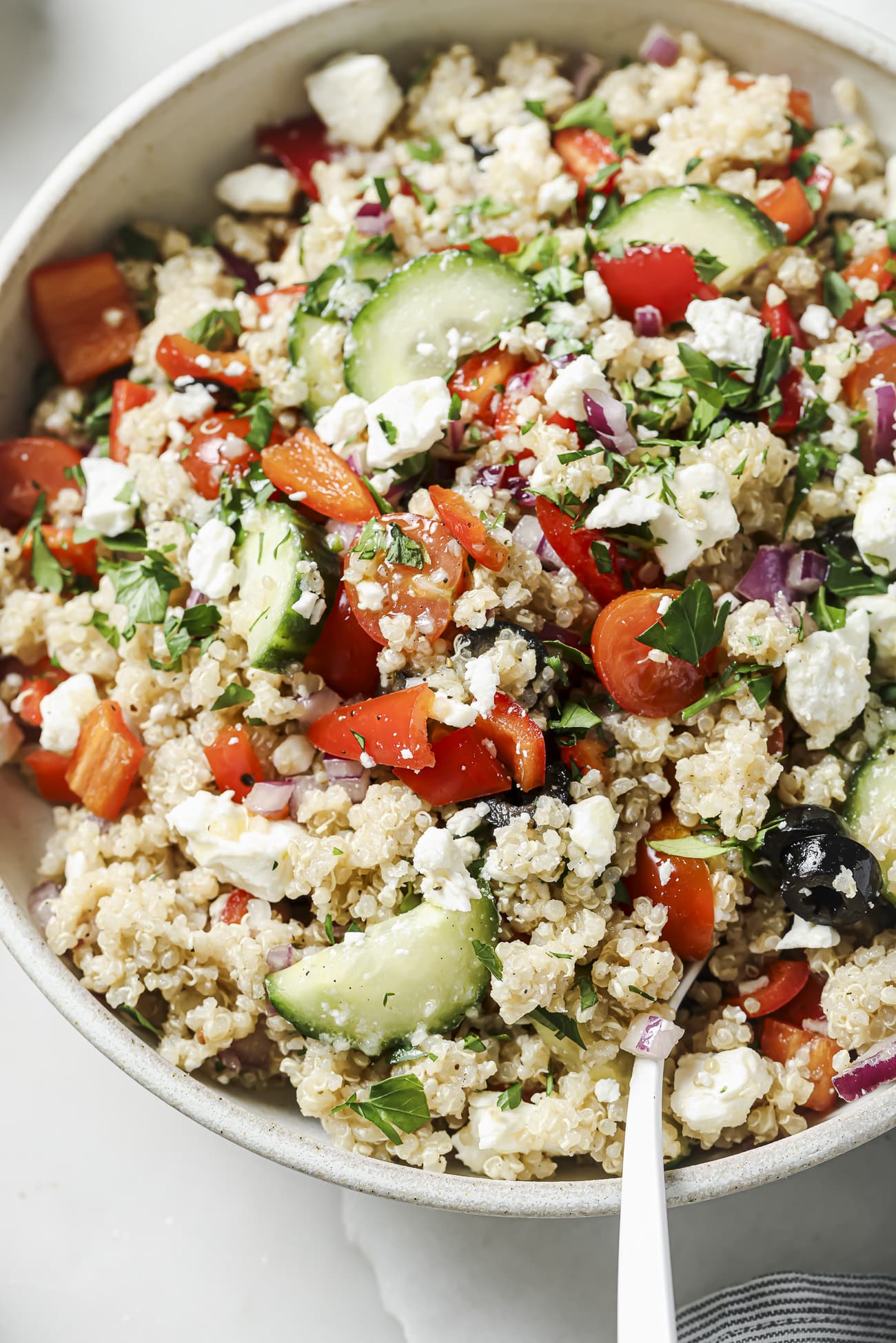 Close up of Greek quinoa salad in a white bowl.