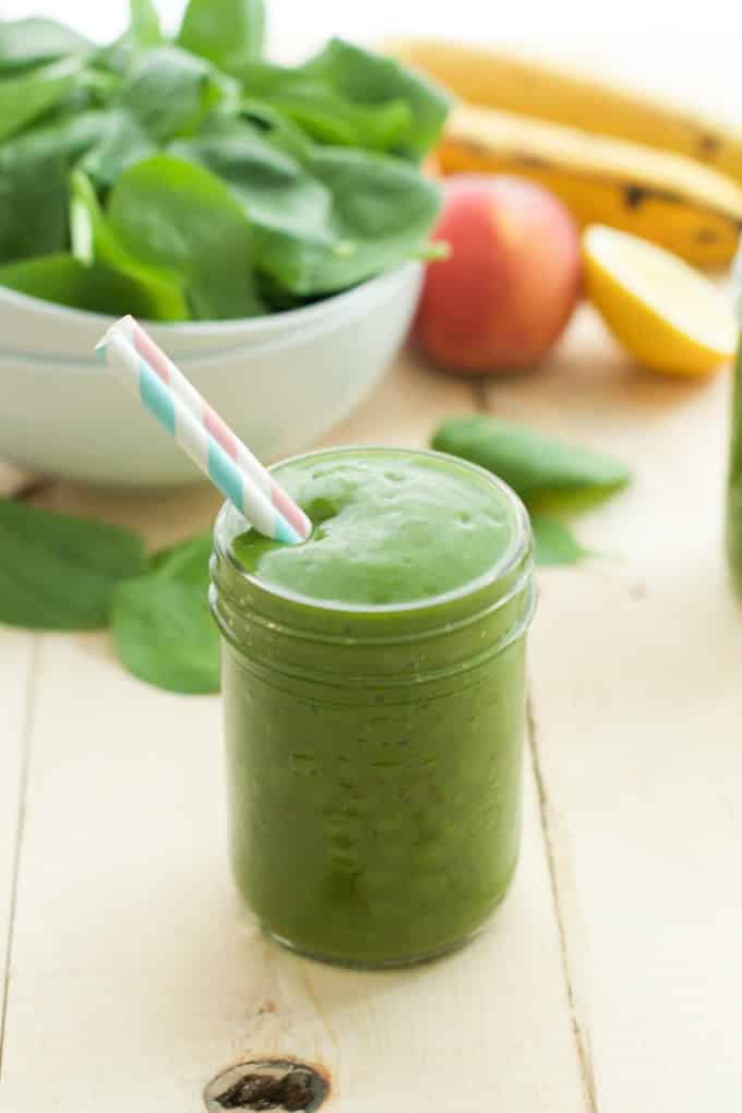 close up of a green smoothie in a mason jar with a straw 