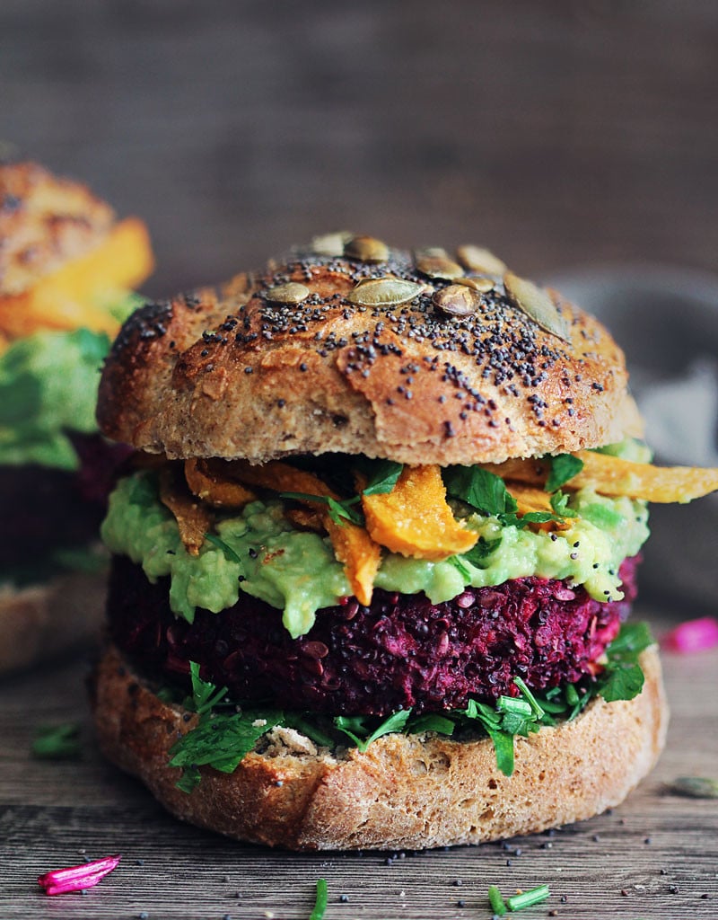 A side view of a colorful veggie burger with avocado and a poppyseed bun.