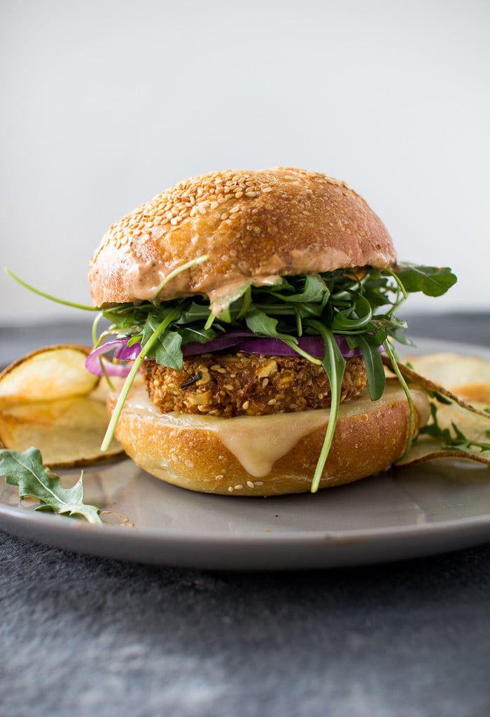 CRUNCHY CHICKPEA BURGERS A side view of a crunchy chickpea burger with onions and arugula on a sesame bun.