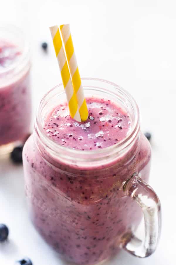 A mason jar of blueberry banana smoothie with two yellow striped straws.
