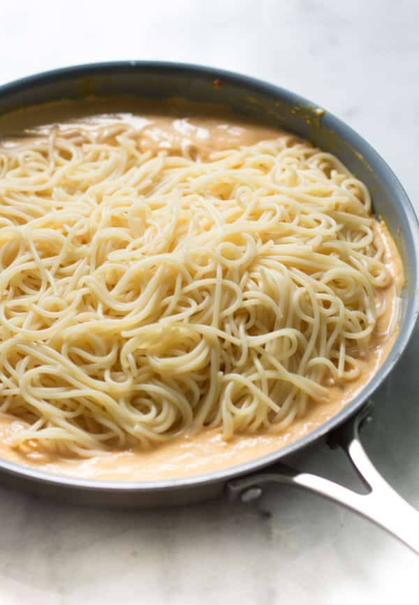 Pasta added to the pumpkin alfredo sauce in the skillet.