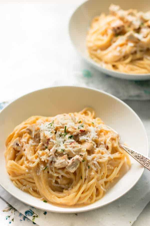 A bowl of pumpkin alfredo sauce pasta with a fork in it.