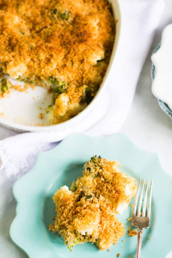 A plate of cheesy broccoli cauliflower bake beside the casserole dish.