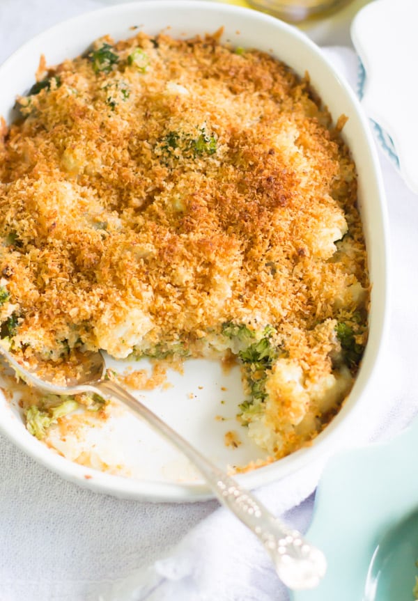 A casserole dish of cheesy broccoli cauliflower bake with a section spooned out.