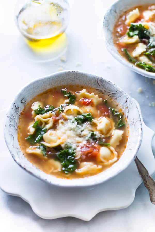 overhead view of a white bowl containing kale tomato tortellini soup