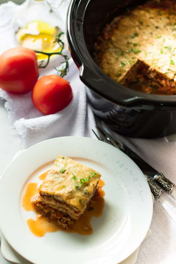 A slice of slow cooker zucchini lasagna on a plate beside a slow cooker.