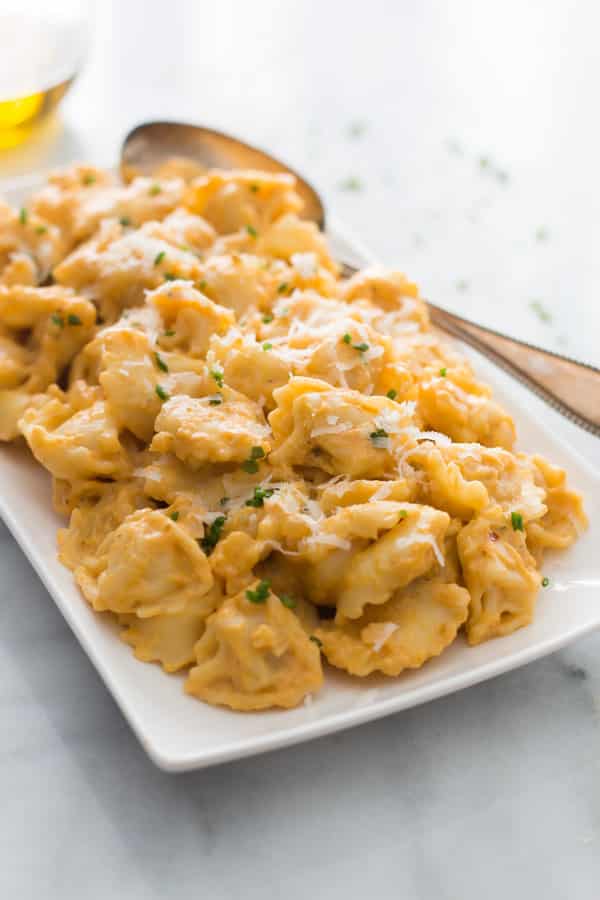 A platter of tortellini pumpkin sauce with a spoon.