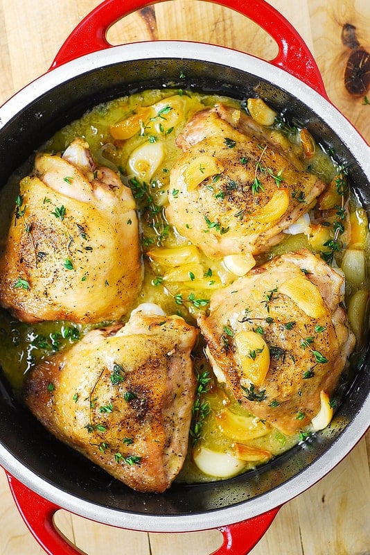 An overhead view of Garlic Thyme Chicken Thighs garnished with fresh thyme in a red Dutch oven.