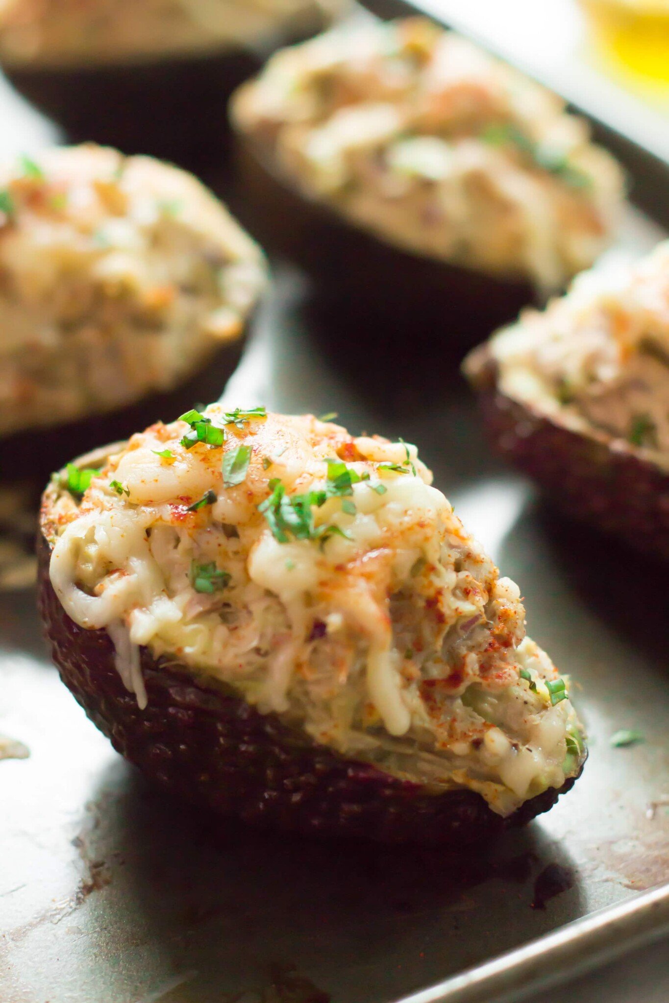 A closeup of avocado halves filled with tuna and topped with mozzarella cheese.