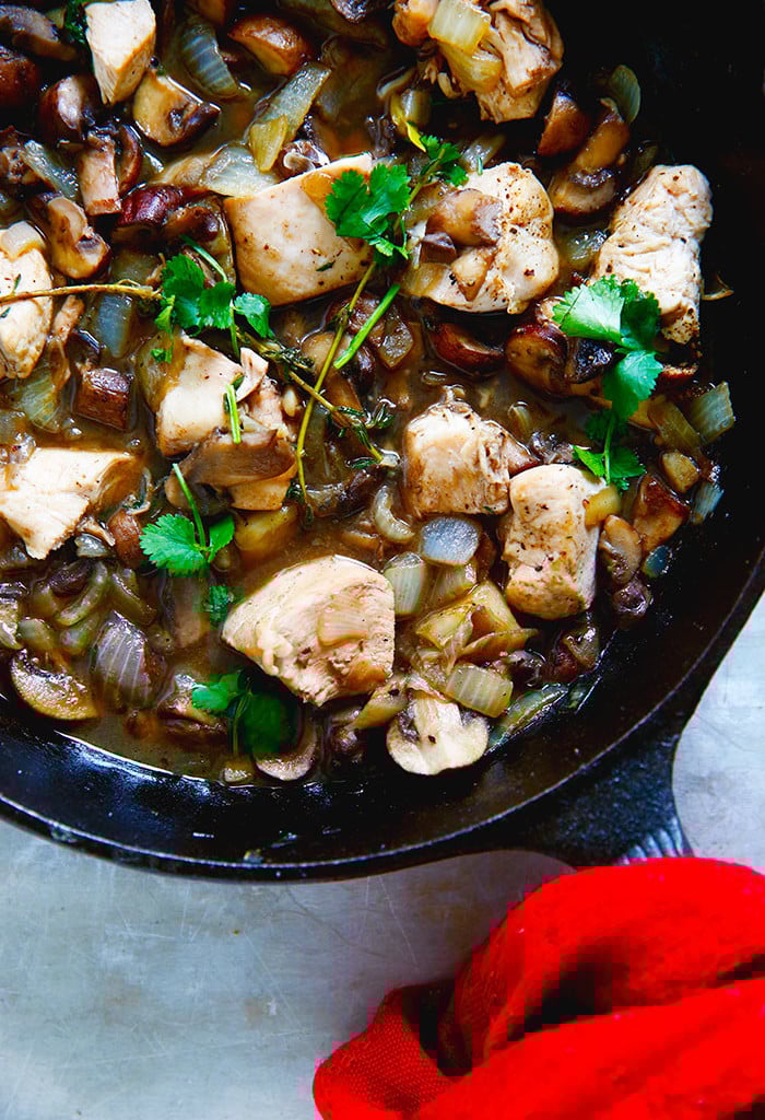 A close-up of Chicken in Mushroom Sauce garnished with fresh herbs in a large black skillet.