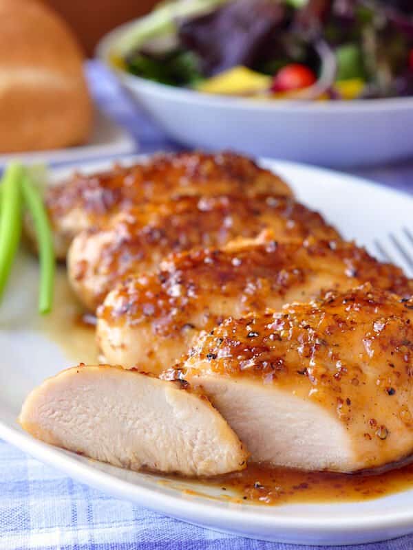 Honey Dijon Garlic Chicken Breasts on a white plate with a slice cut from the first one.