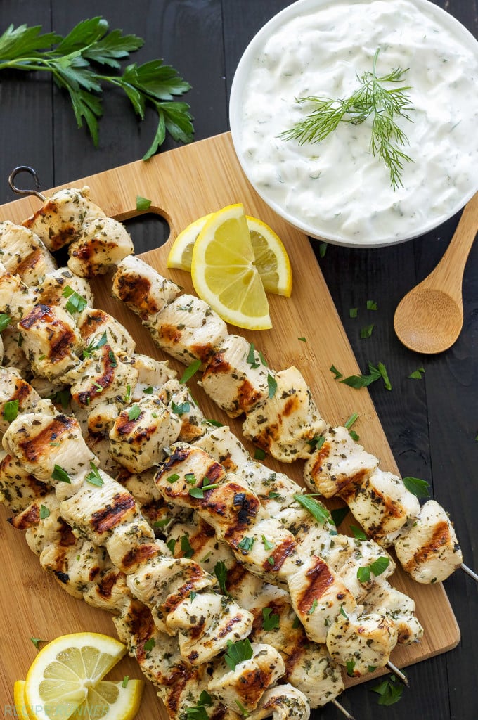 Greek Lemon Chicken Skewers on a wooden cutting board with a bowl of tzatziki sauce on the side.
