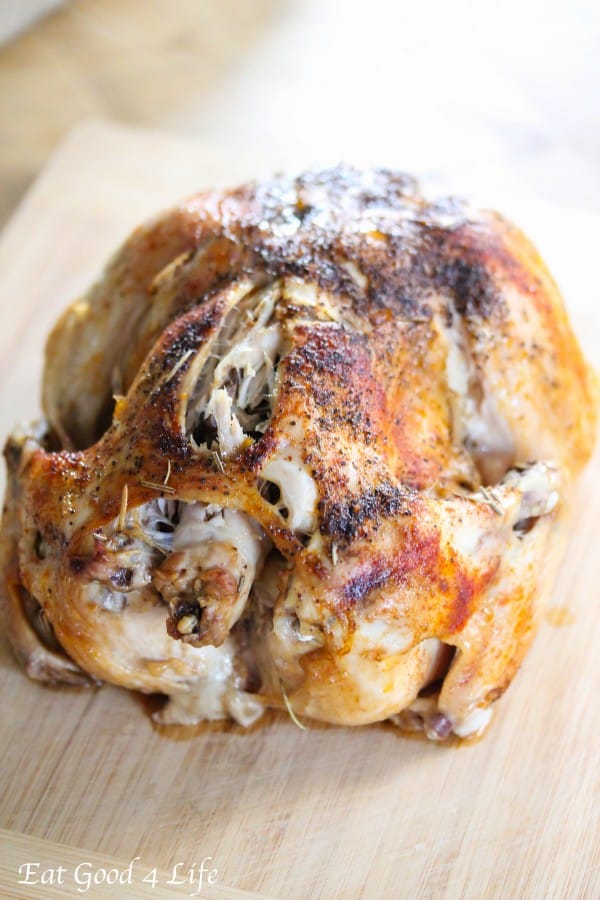 A close-up of a whole slow cooker roasted chicken on a wooden cutting board.