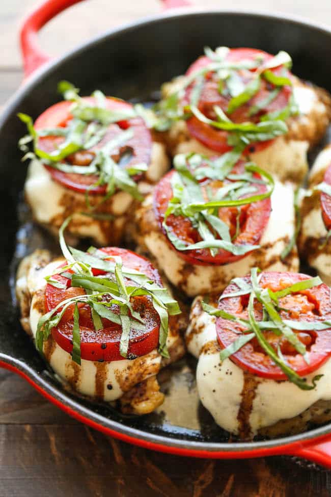 A close-up view of caprese chicken breasts topped with tomatoes and fresh basil in a skillet.