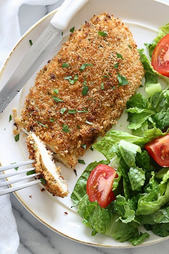 An overhead view of a mustard and herb coated chicken breast with a small salad on the side.