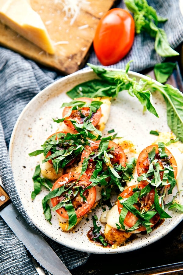 An overhead view of balsamic caprese chicken topped with tomatoes and fresh basil on a blue tea towel.