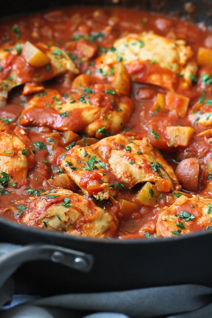 One-Pot Curry Tomato Chicken & Potatoes garnished with fresh herbs in a skillet.