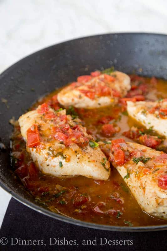 Tuscan Chicken topped with tomatoes and fresh herbs inside of a black skillet.