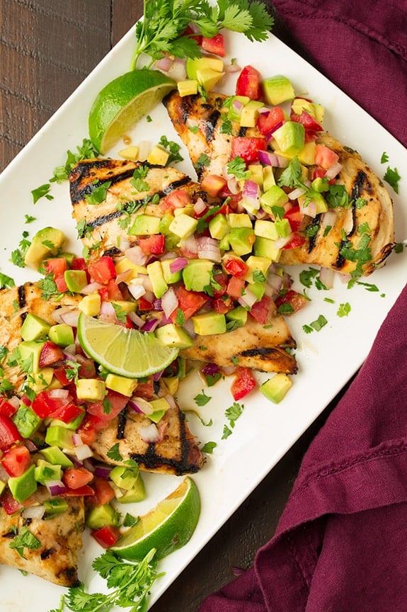 Grilled Cilantro-Lime Chicken with Avocado Salsa on a white plate with lime wedges around the edge of the plate.