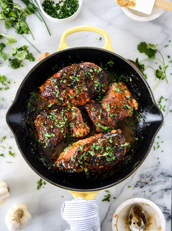 An overhead view of honey Dijon chicken topped with fresh herbs in a black skillet.