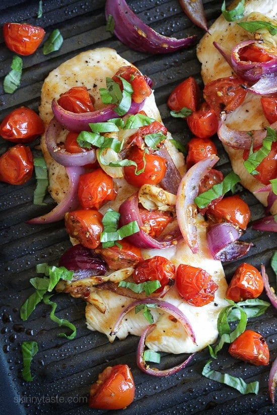 An overhead view of chicken topped with roasted tomatoes, onions, and basil on a grill pan.