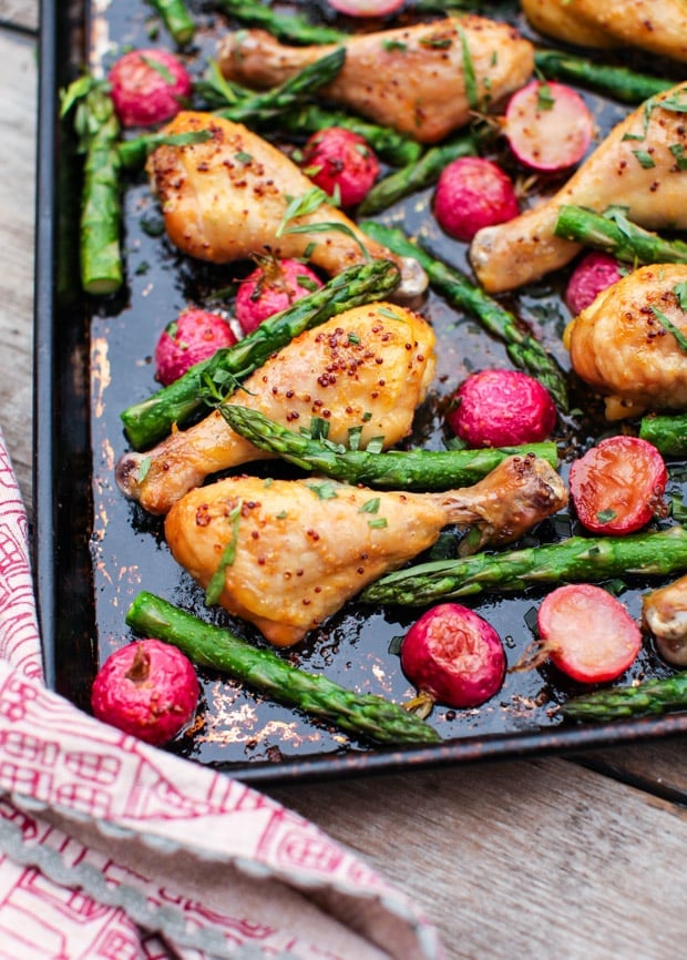 Maple Mustard Chicken Drumsticks with radishes and asparagus on a baking sheet.