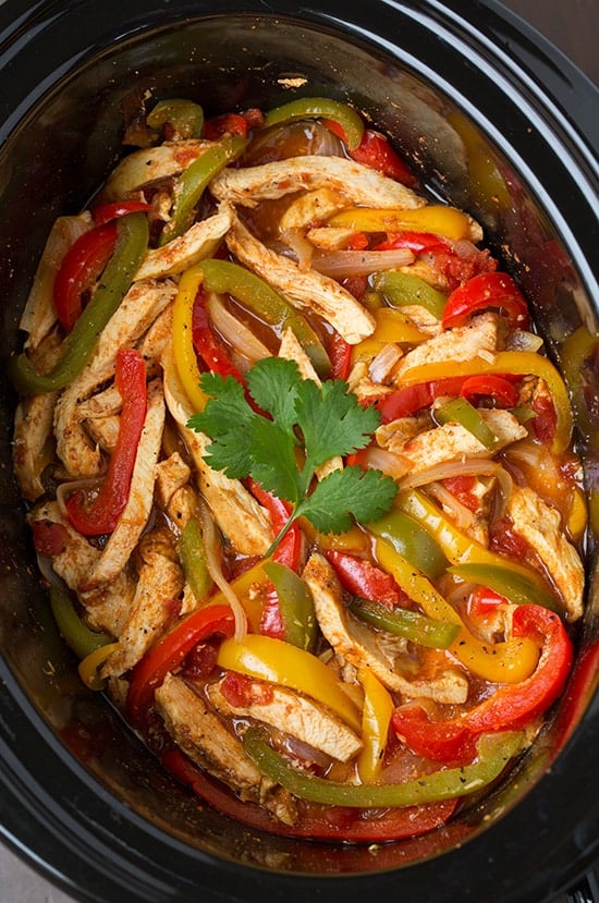 An overhead view of chicken and bell peppers topped with a sprig of cilantro in a slow cooker.