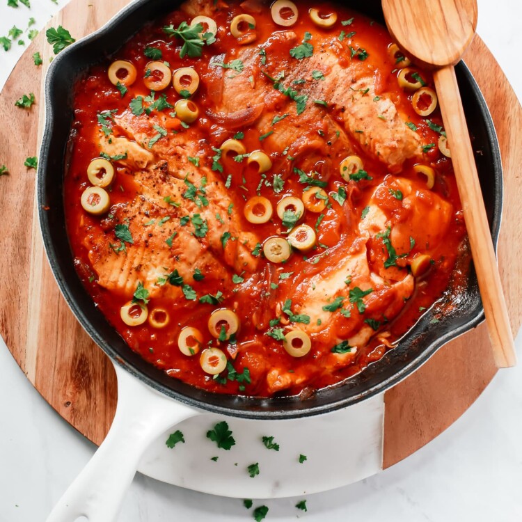 overhead view of a white skillet containing tilapia in a tomato sauce