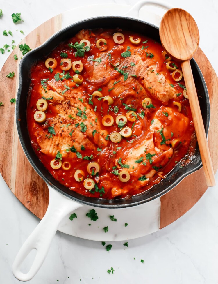 overhead view of a white skillet containing tilapia in a tomato sauce.