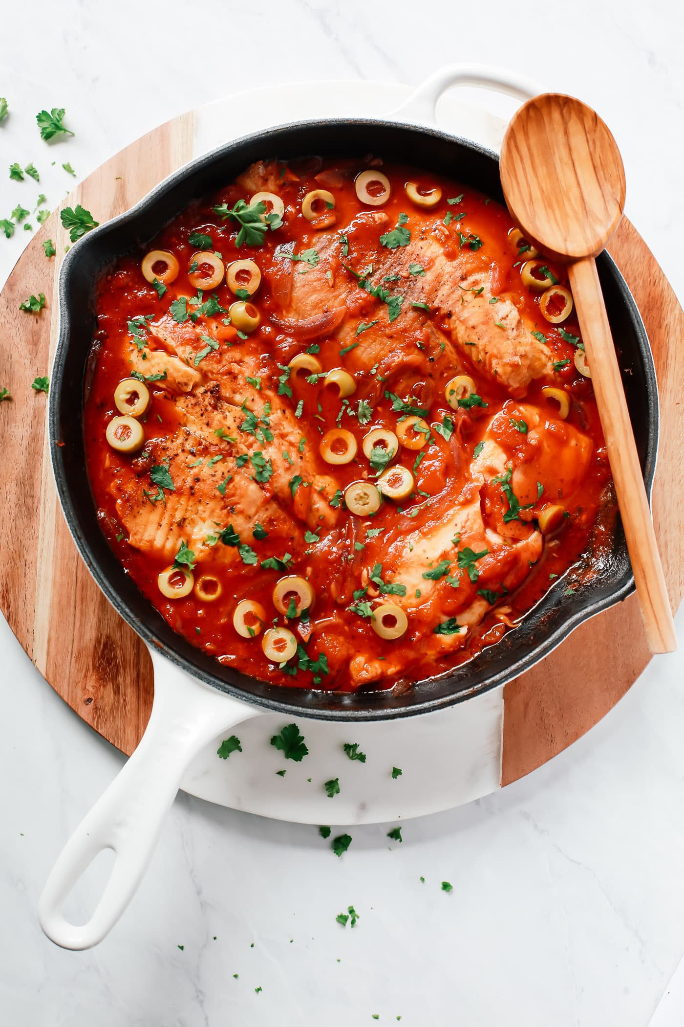 overhead view of a white skillet containing tilapia in a tomato sauce.