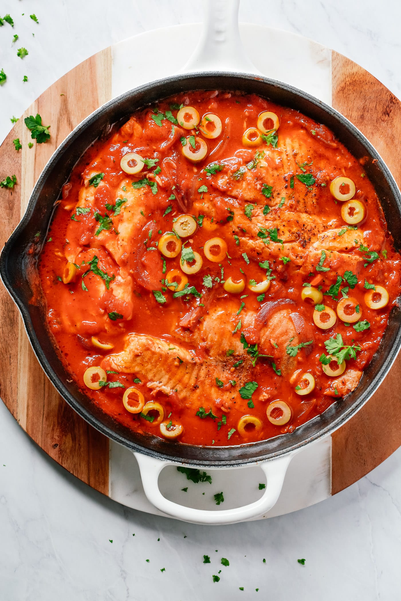 overhead view of a white skillet containing tilapia in a tomato sauce.