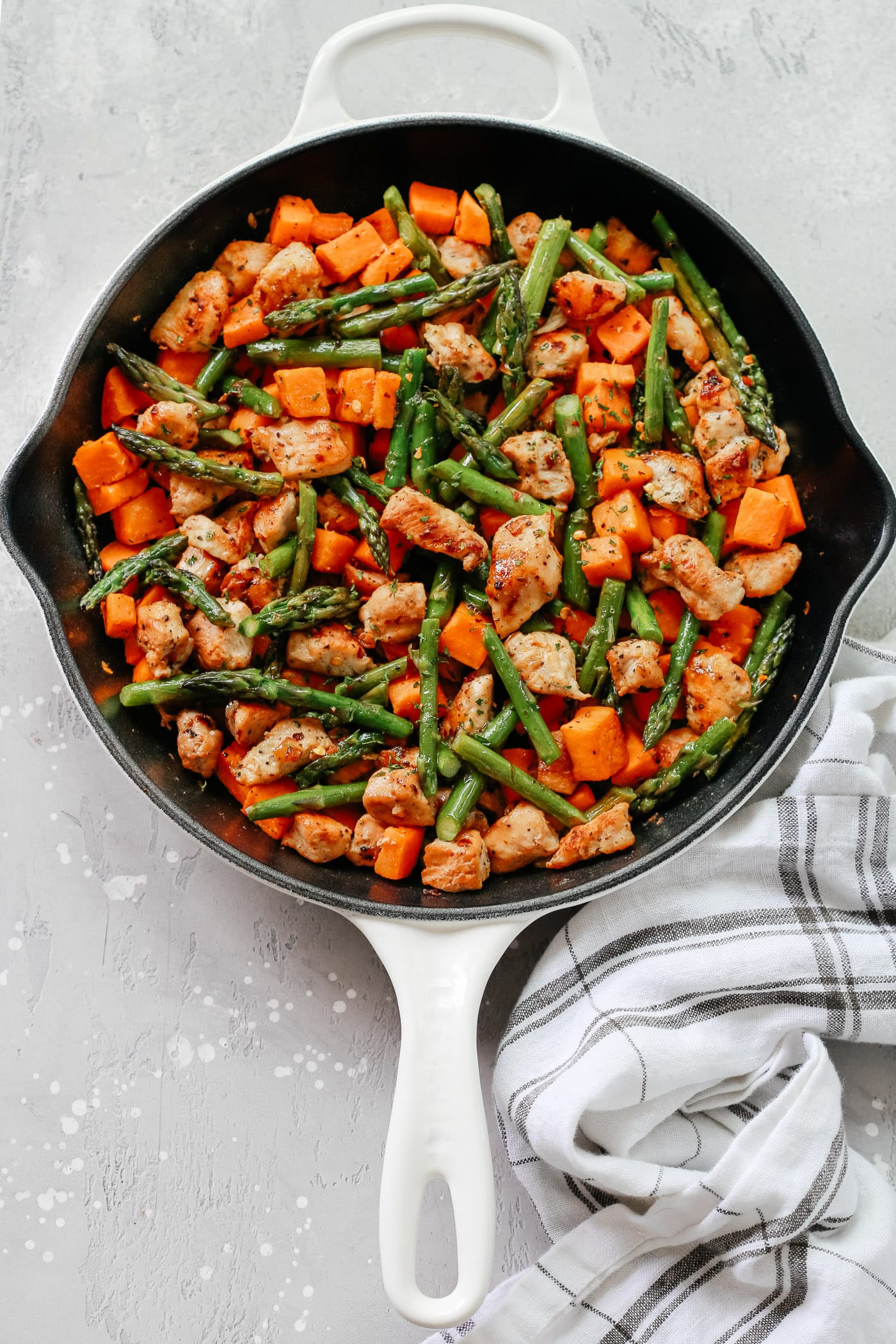 White skillet with asparagus, sweet potato, and chicken.