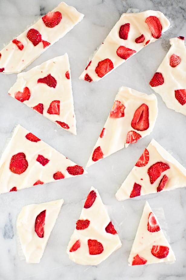 Pieces of white frozen yogurt bark with red strawberries in it.