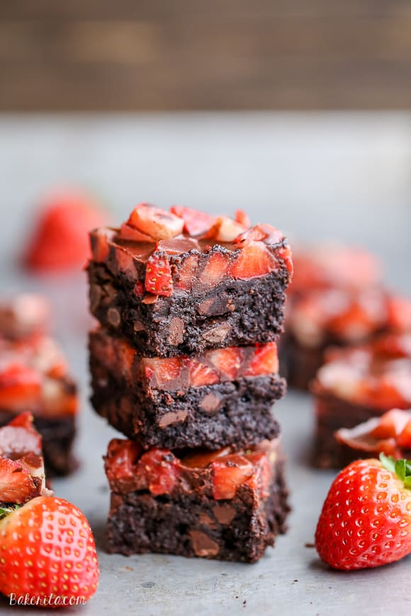 A stack of three chocolate covered strawberry brownies with whole strawberries next to it.