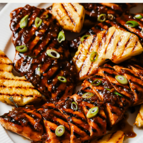 Grilled Pineapple Chicken breast slices with caramelized grill marks, topped with chopped green onions and served alongside grilled pineapple wedges on a white plate. Text overlay reads “Grilled Pineapple Chicken: Juicy and caramelized with grill marks.”.