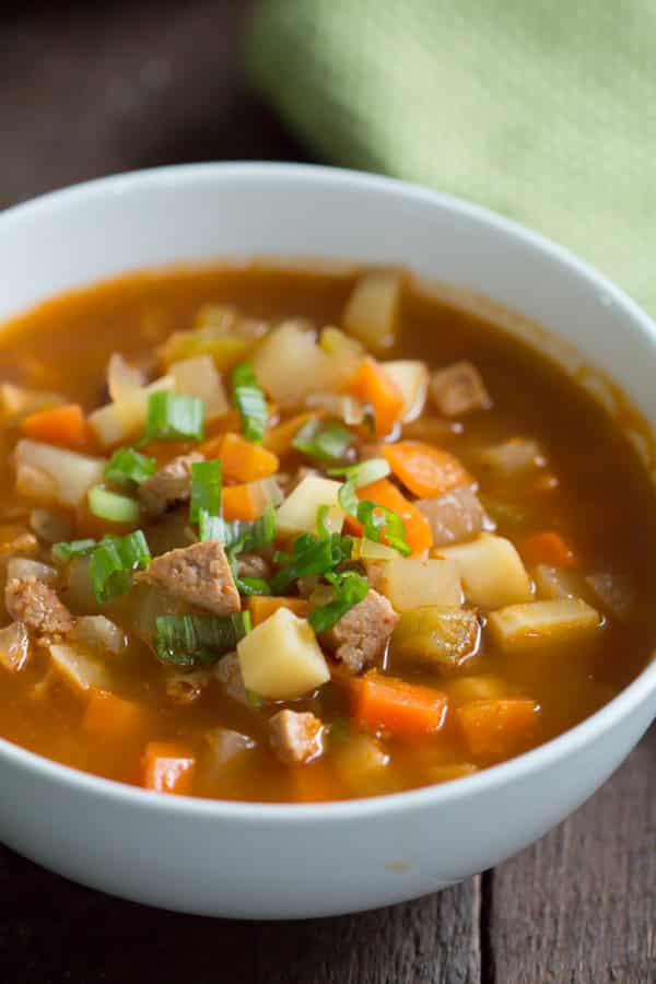 close-up of a sausage and vegetable soup in a white bowl