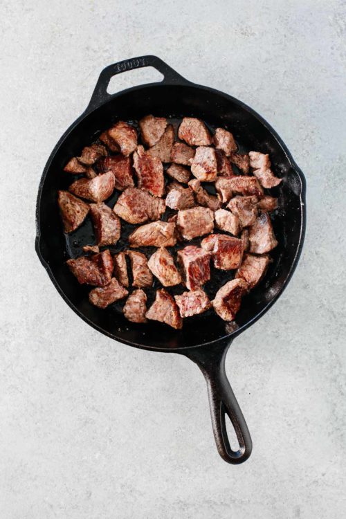 overhead view of a cast iron skillet containing steak bites