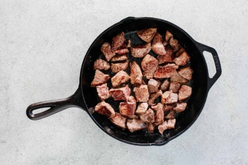 overhead view of a cast iron skillet containing steak bites