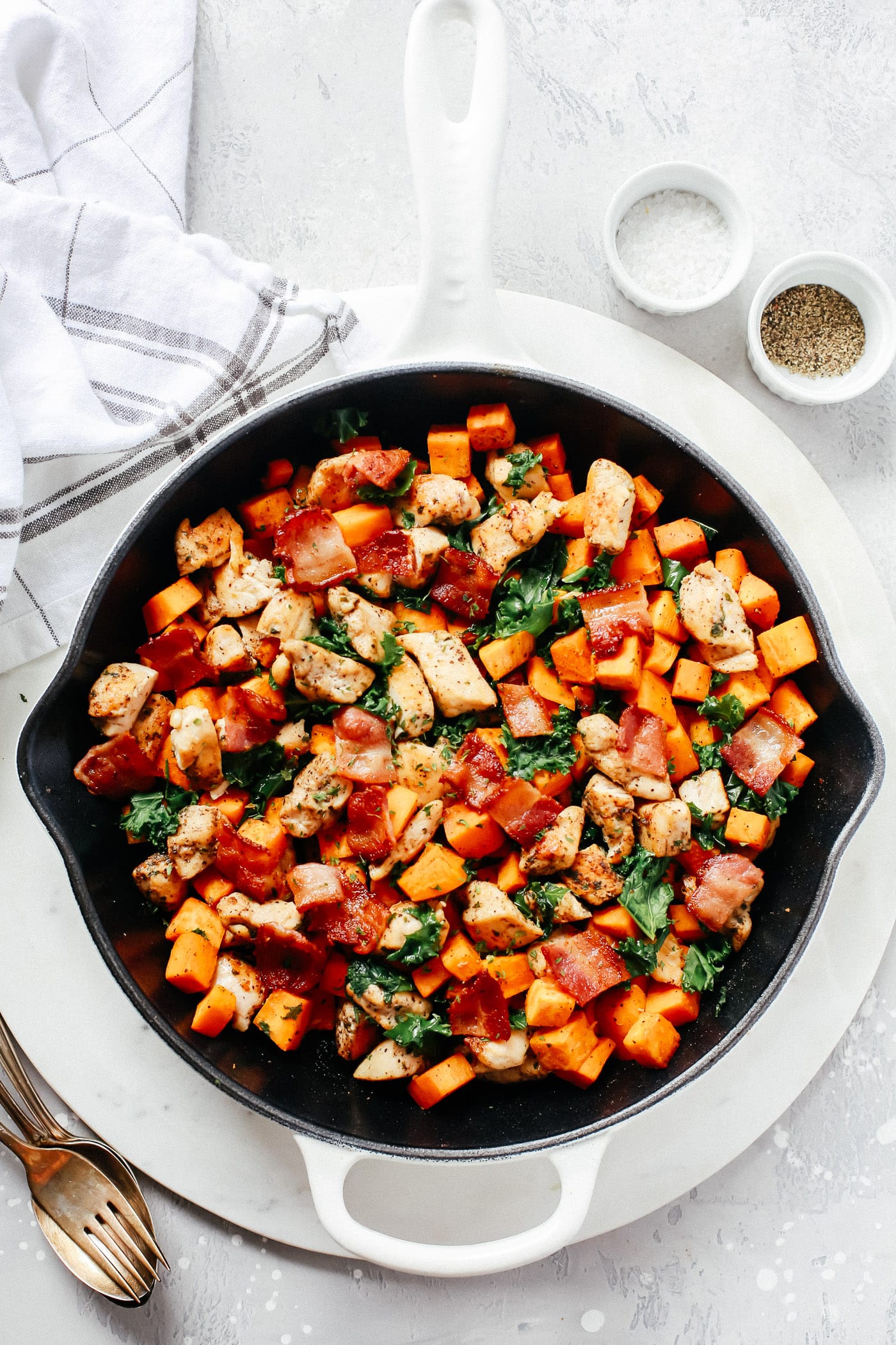 A white skillet with sweet potato chicken and kale.