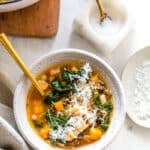 White bean and kale soup in a serving bowl with shredded parmesan cheese topping.