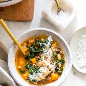 White bean and kale soup in a serving bowl with shredded parmesan cheese topping.