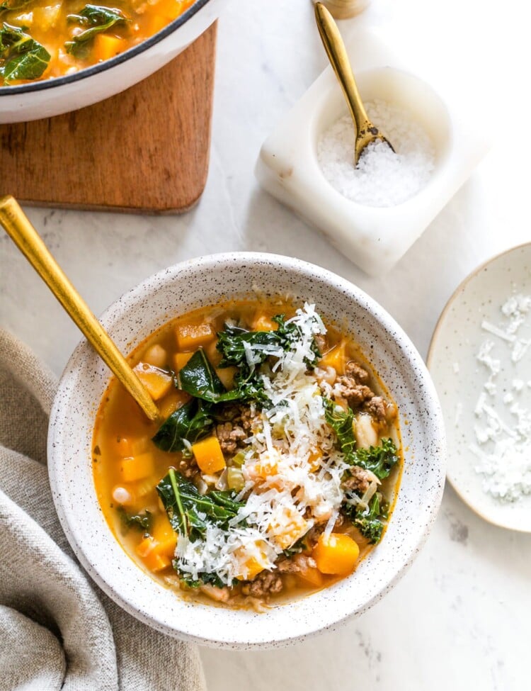 White bean and kale soup in a serving bowl with shredded parmesan cheese topping.
