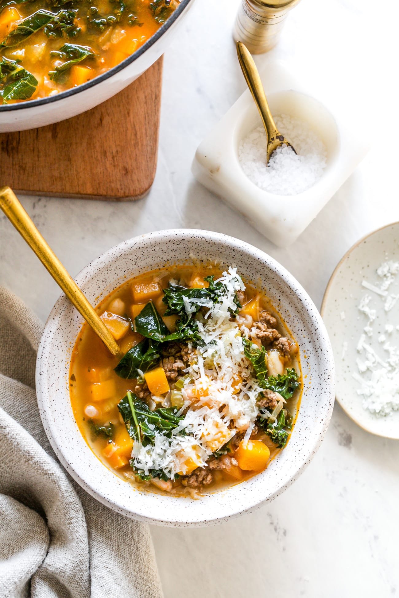 White bean and kale soup in a serving bowl with shredded parmesan cheese topping.