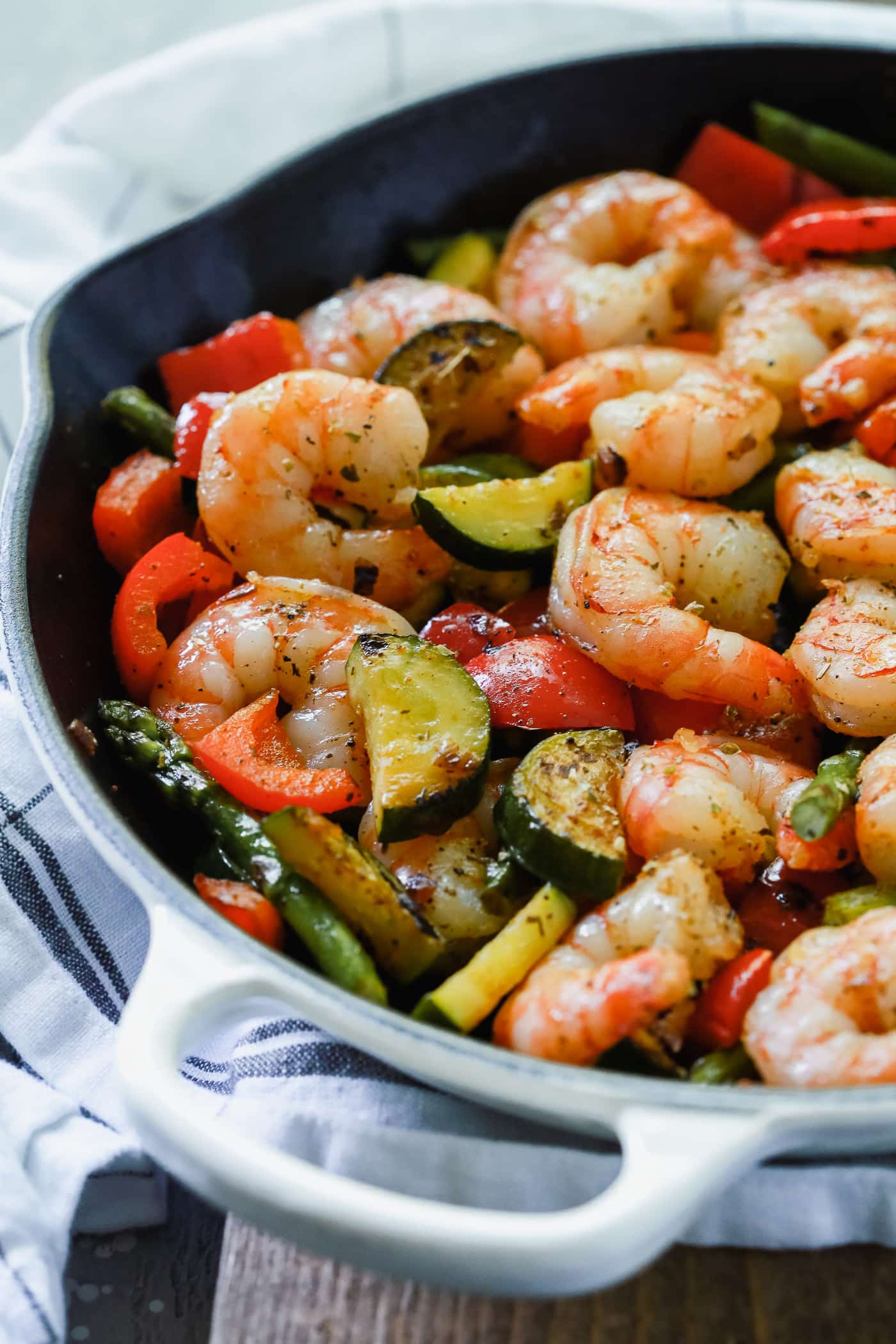Overhead view of a cast iron with shrimp, bell peppers, zucchini, and asparagus. 